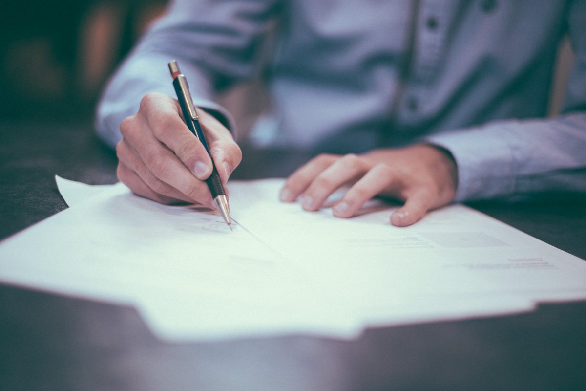 A hand holding a pen over a printed document on a dark desk