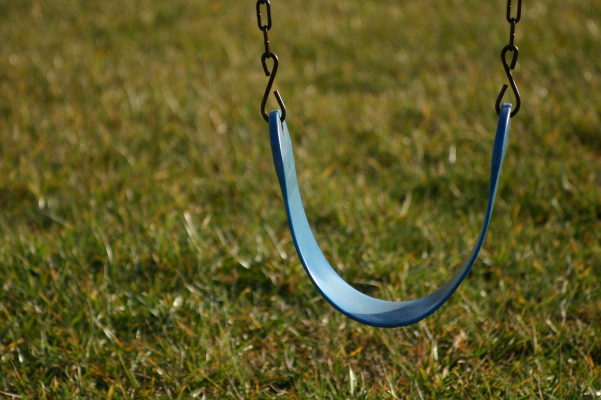 An empty blue swing seat hanging on chains over a grass lawn