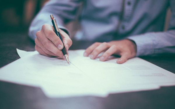 A hand signing a document with a pen